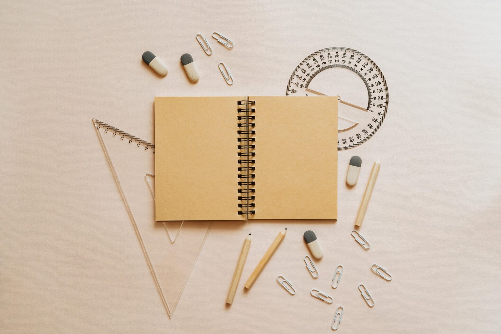 Flat lay of school stationery including a notebook, pencils, and geometry tools on a beige background.